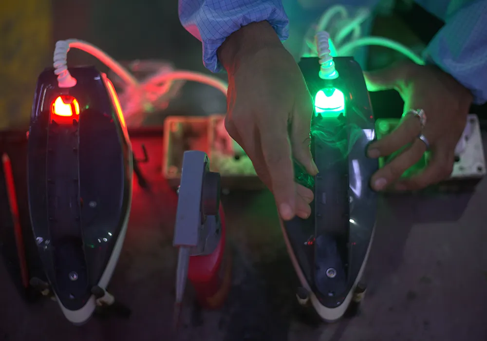 Hands testing irons on a bench, with red and green indicator lights